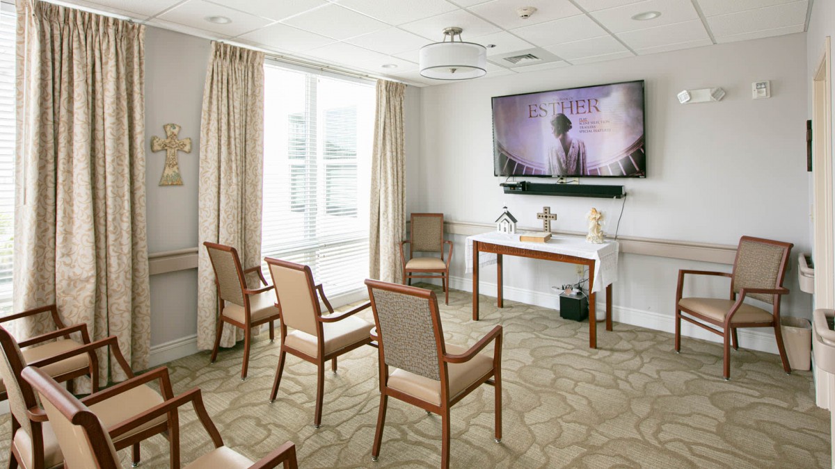 A neatly arranged meeting room with chairs facing a large television on the wall.