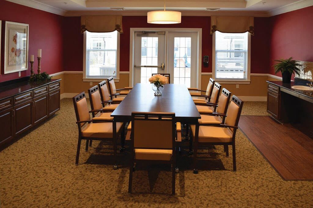 A well-lit dining room featuring a long table and chairs, with windows allowing natural light to enter.