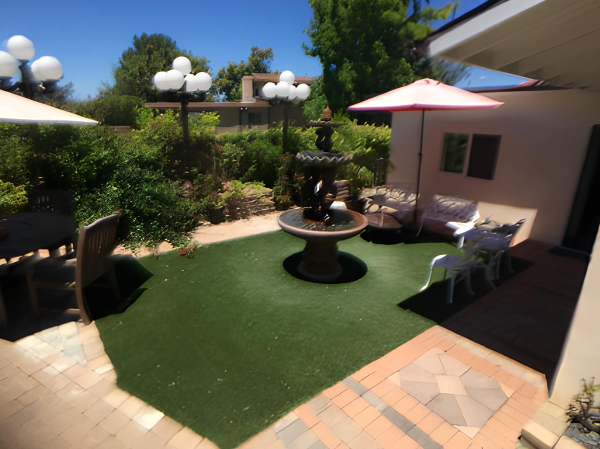 A sunny garden with a central fountain surrounded by artificial grass and patio furniture.