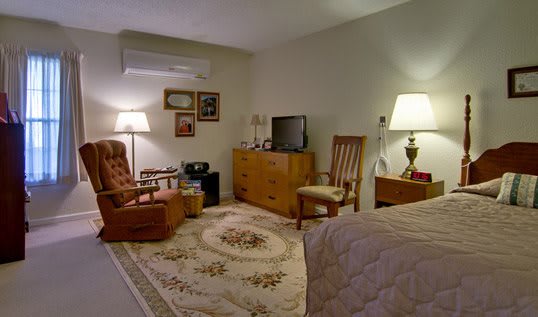 A cozy room with vintage furniture and decor, featuring a television, lamps, and a patterned rug.