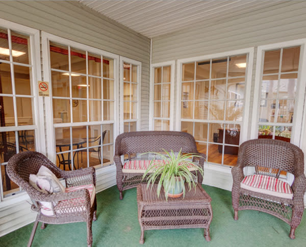A cozy porch with wicker furniture and a potted plant, surrounded by large windows.
