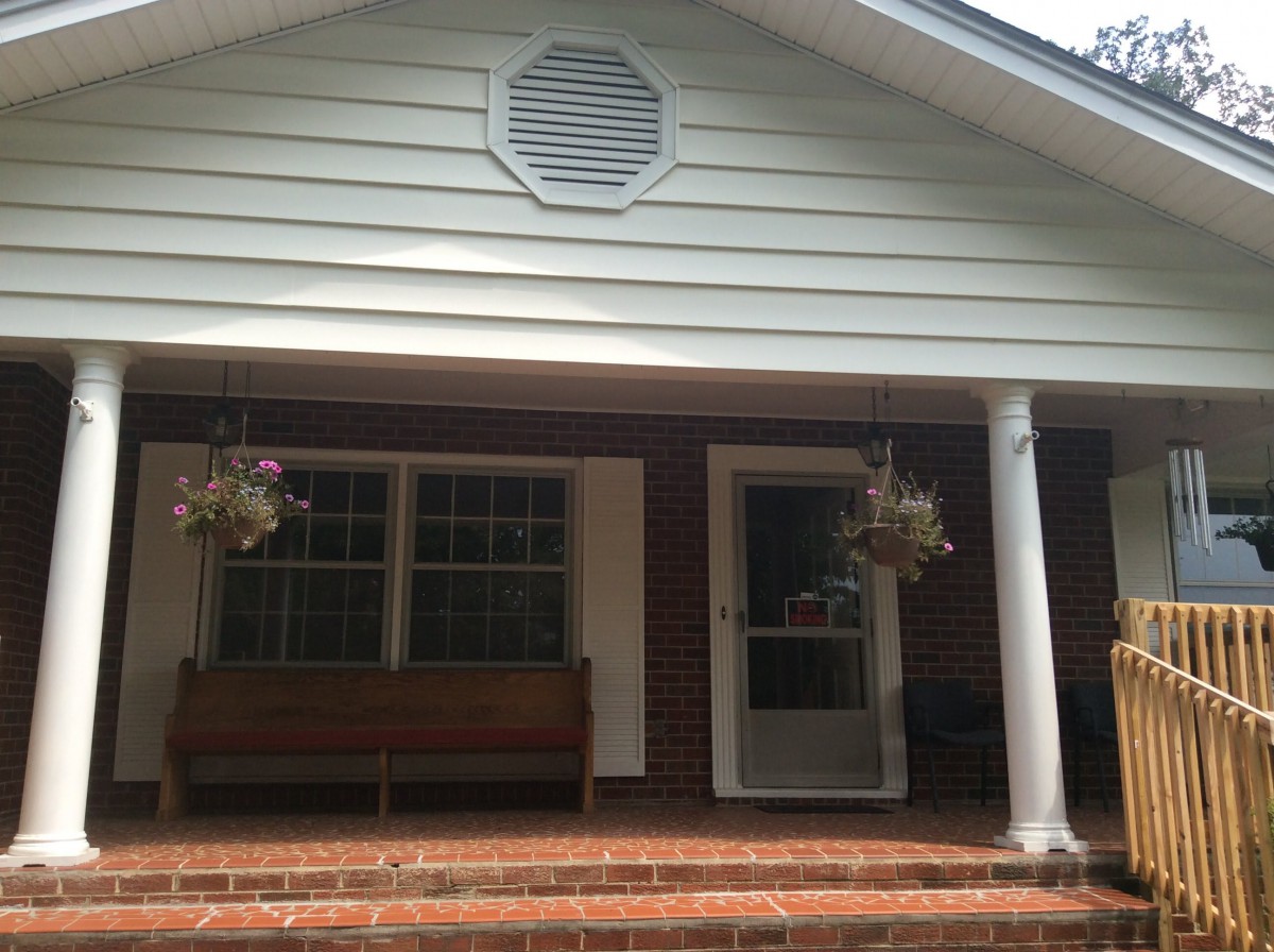 A cozy porch with a bench and hanging plants.