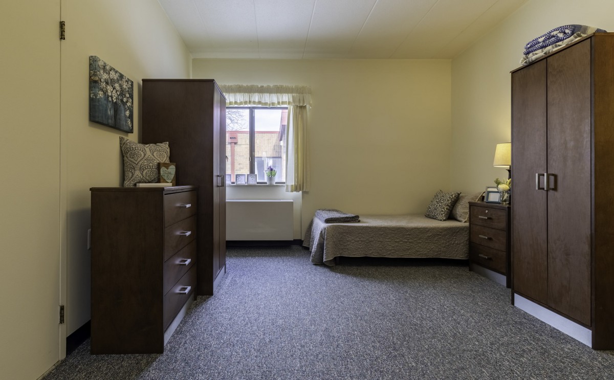 A simple bedroom with a single bed, dresser, and window.