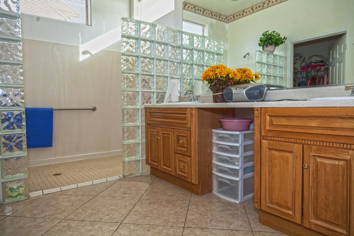 A bathroom featuring a wooden vanity, glass block divider, and decorative flowers.