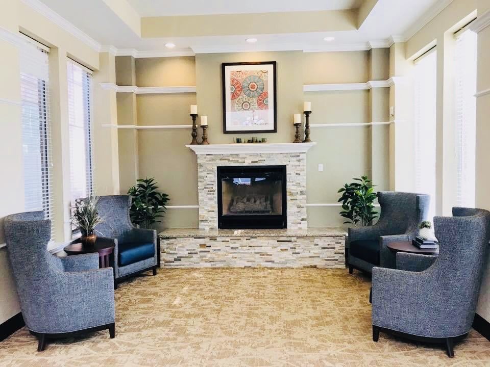 A cozy living room with a fireplace, surrounded by armchairs and indoor plants.