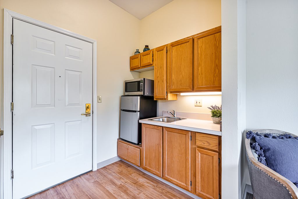 A compact apartment kitchen featuring wooden cabinets, a microwave, refrigerator, and sink.
