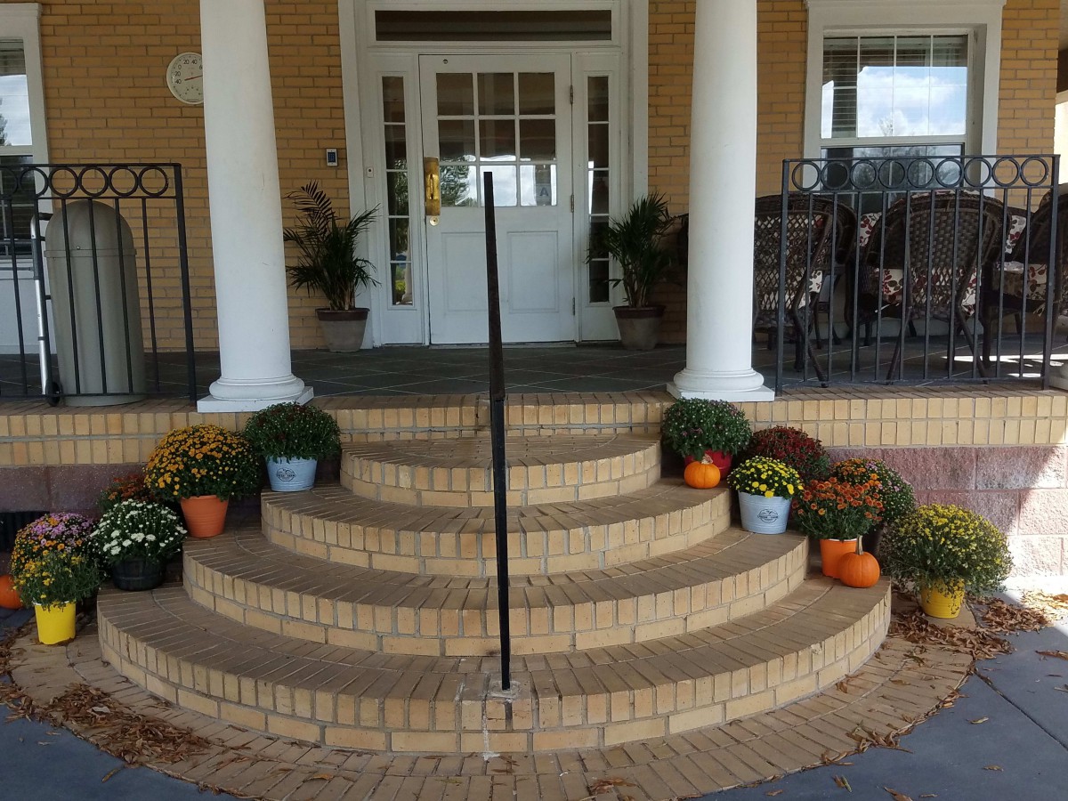 A front porch with curved brick steps decorated with pumpkins and flowers, framed by white columns.