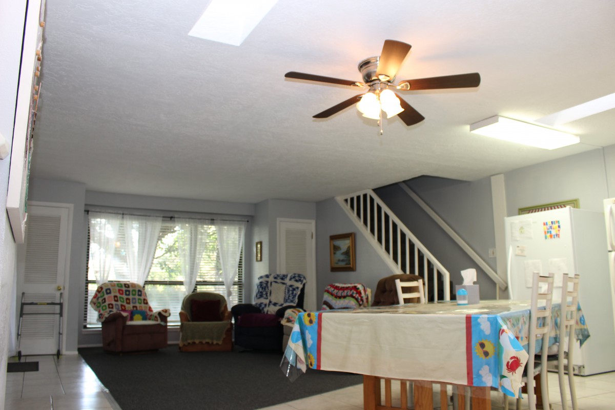A spacious living room with a ceiling fan, staircase, and comfortable furniture.