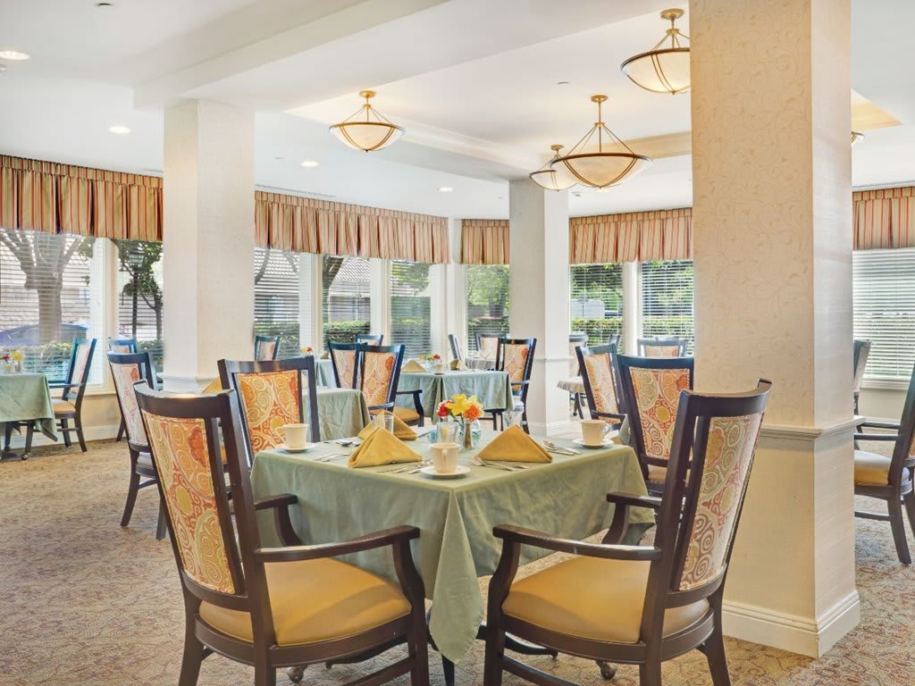 A well-lit dining room with elegantly set tables and chairs, featuring large windows that allow natural light to flood the space.