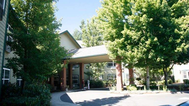 A building entrance surrounded by lush green trees on a sunny day.