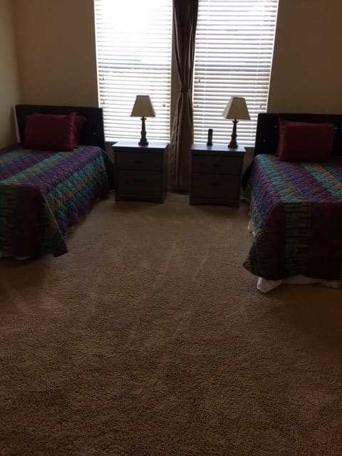 A neatly arranged bedroom with twin beds, lamps, and nightstands by the windows.