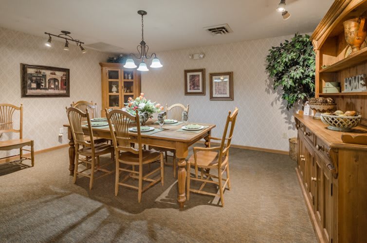 A cozy dining room with a wooden table and chairs, illuminated by overhead lighting and adorned with decorative elements.