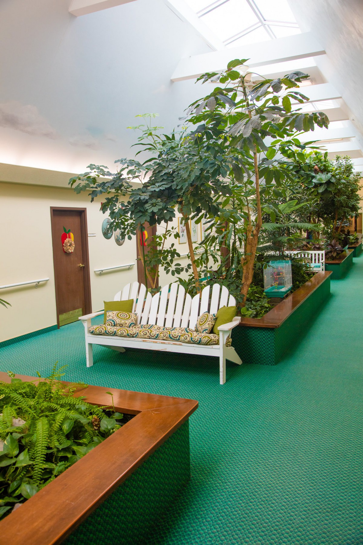A tranquil indoor lobby with lush plants, a green carpet, and a cozy bench for relaxation.
