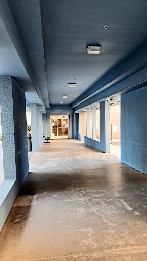 A spacious corridor featuring blue walls and large windows, leading to an entrance.