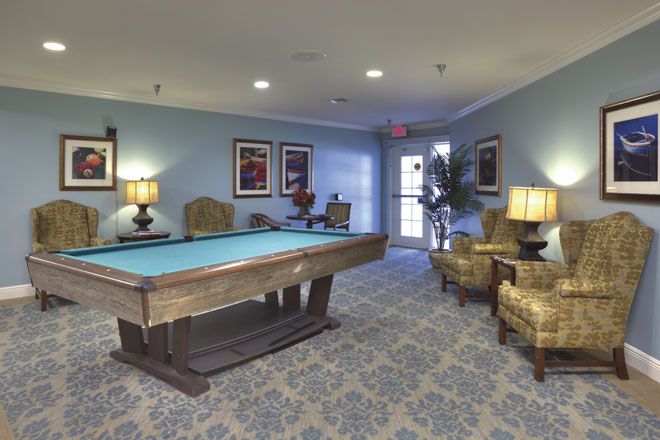 A cozy billiard room with a pool table and comfortable seating areas, decorated with lamps and artwork on the walls.