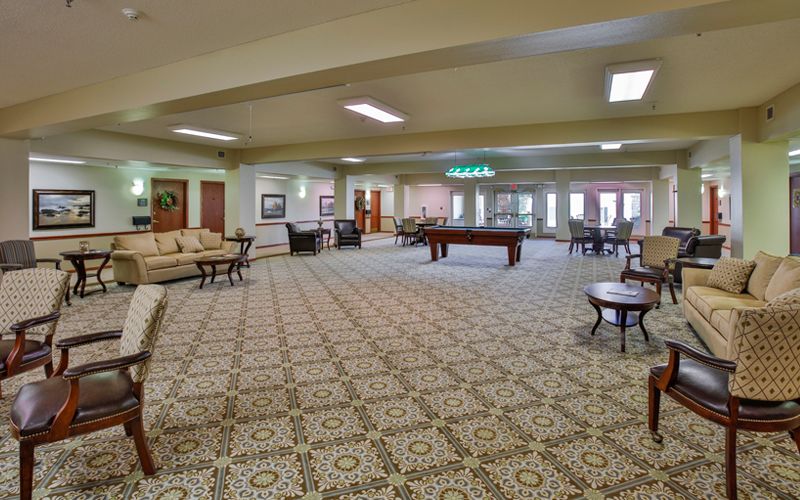 A spacious and well-lit common area featuring comfortable seating, tables, and a decorative carpet.