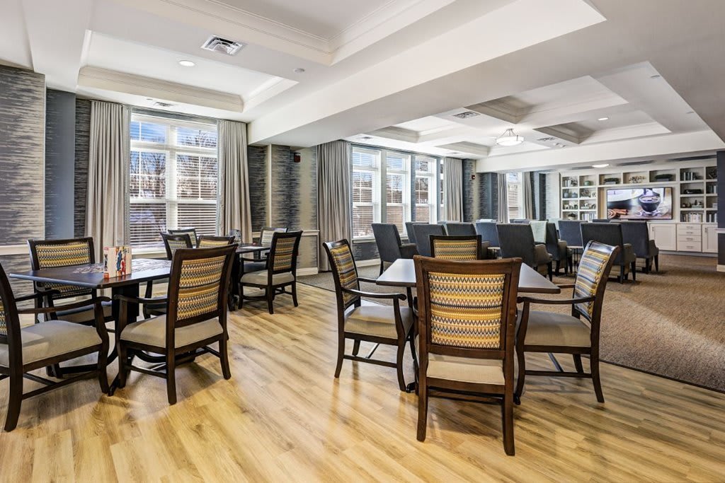 A spacious dining room with wooden tables and chairs, featuring large windows and a wood floor.