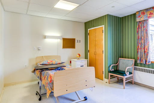 A well-appointed hospital patient room featuring a bed, chair, and warm decor.