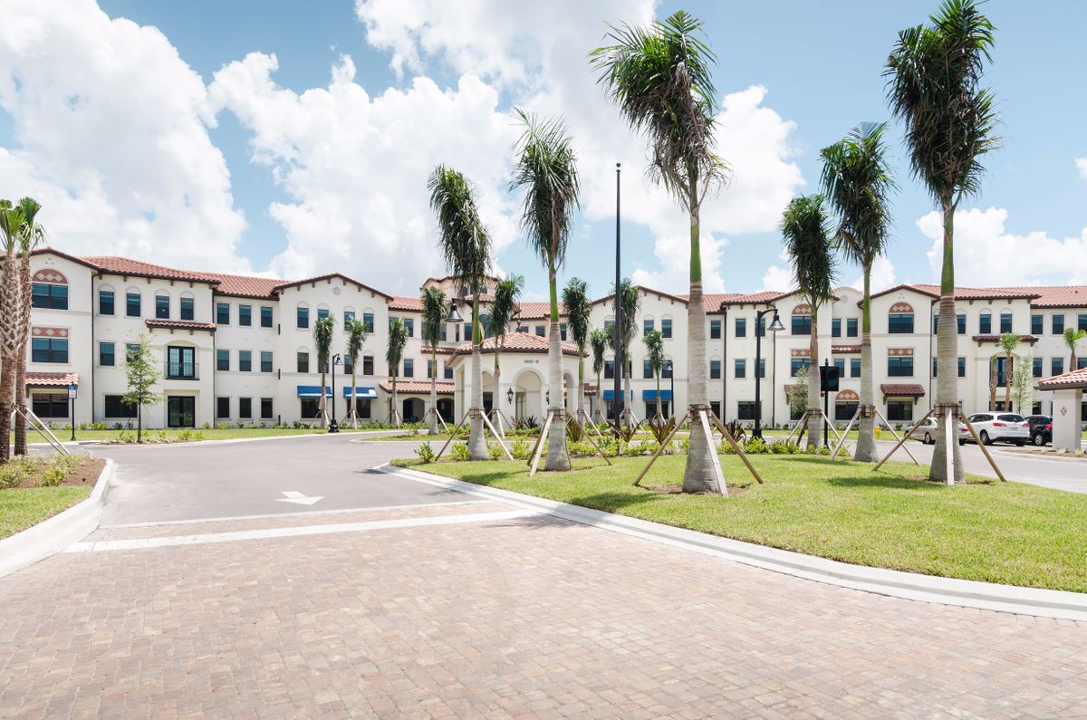 A modern residential building surrounded by palm trees under a clear sky.