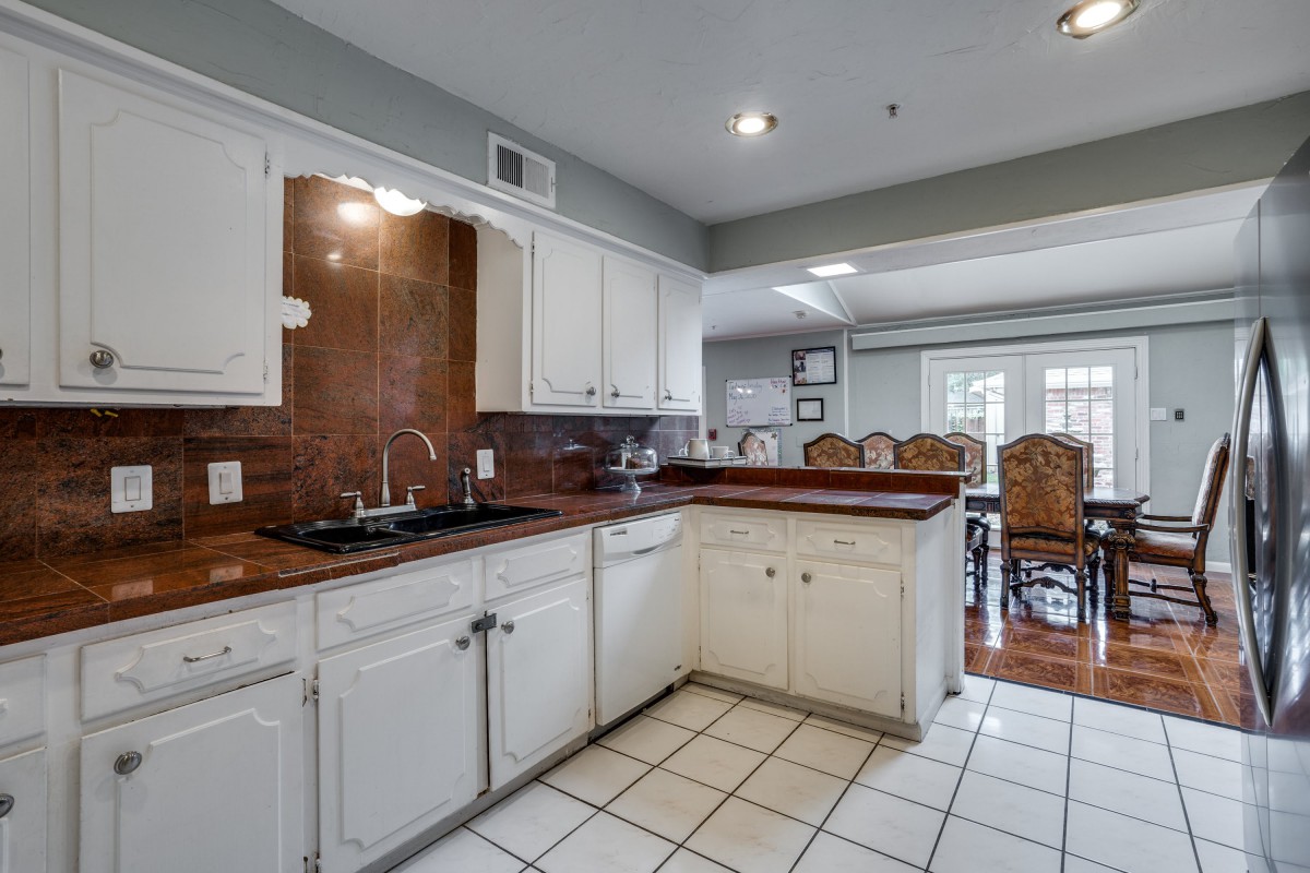 A modern kitchen with white cabinets, a dark countertop, and a view of the dining area.