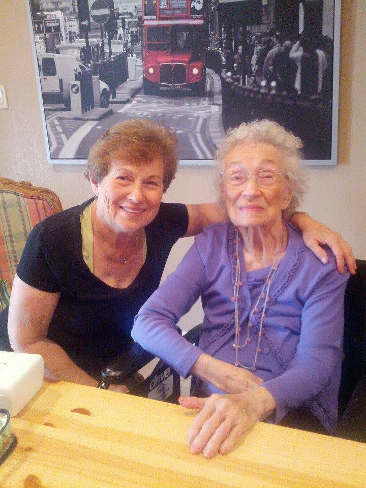 Two elderly women smiling and sitting together indoors.