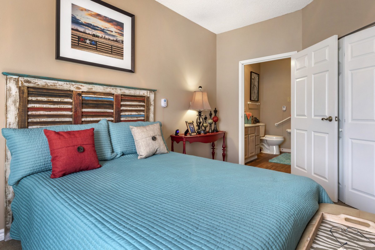 Cozy bedroom with a blue bedspread, decorative pillows, and an open doorway leading to a bathroom.