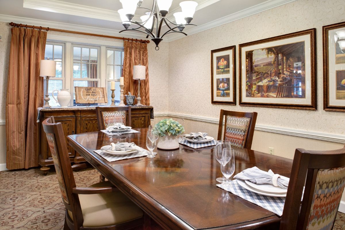 A neatly arranged dining room with a wooden table set for four, featuring a chandelier and framed artwork on the walls.