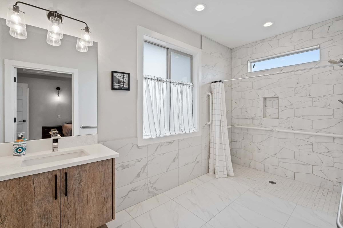 A modern bathroom with a spacious shower, wooden vanity, and elegant lighting.