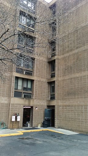 A close-up view of a concrete building featuring multiple windows and a tree in the foreground.