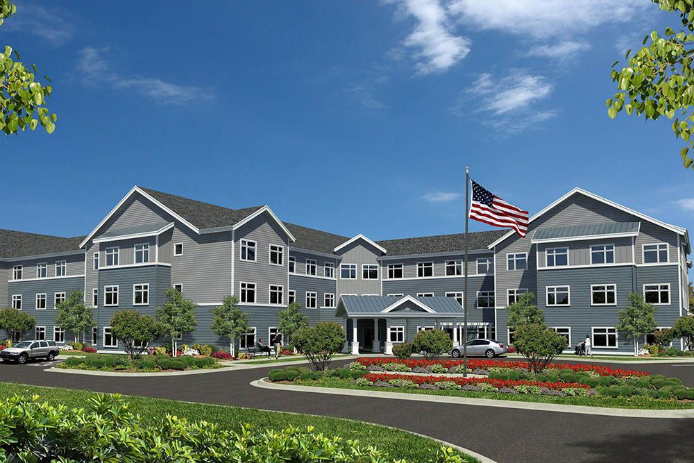 A large residential building with an American flag in front, surrounded by landscaping, under a blue sky with clouds.
