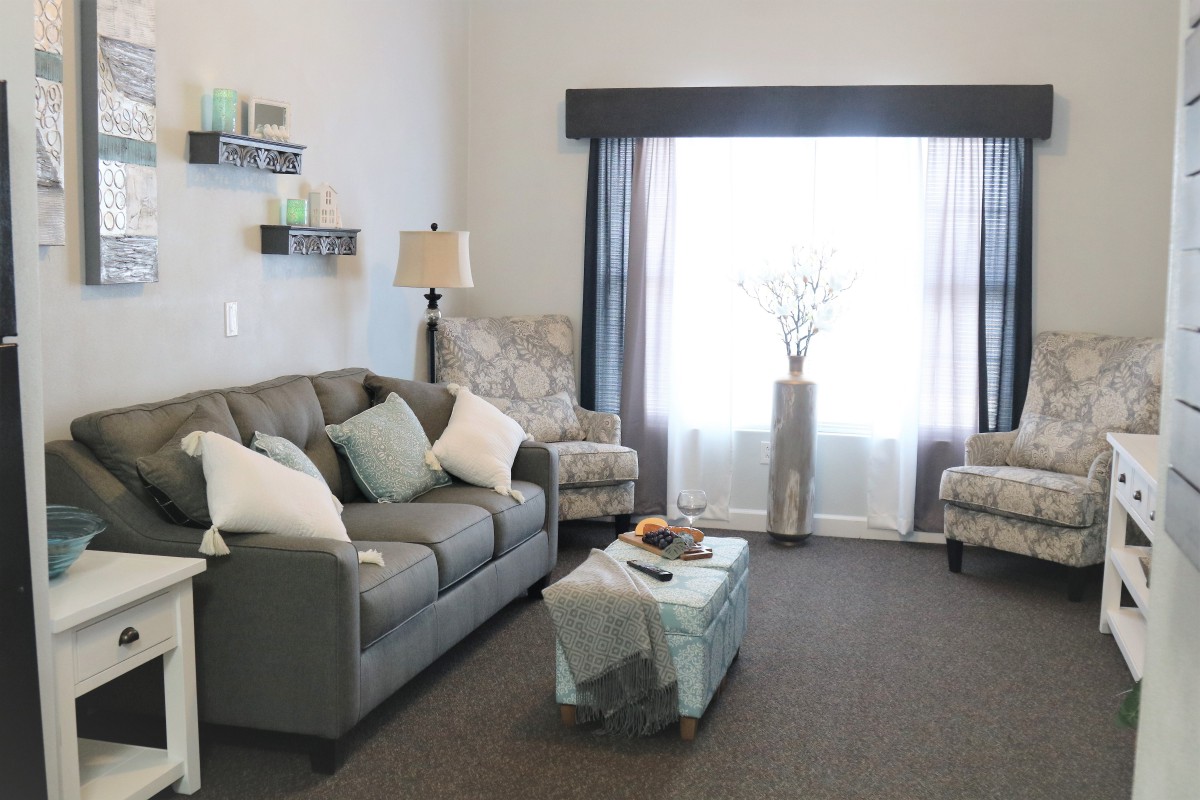 A cozy living room with a gray sofa, armchairs, and a coffee table near a window.
