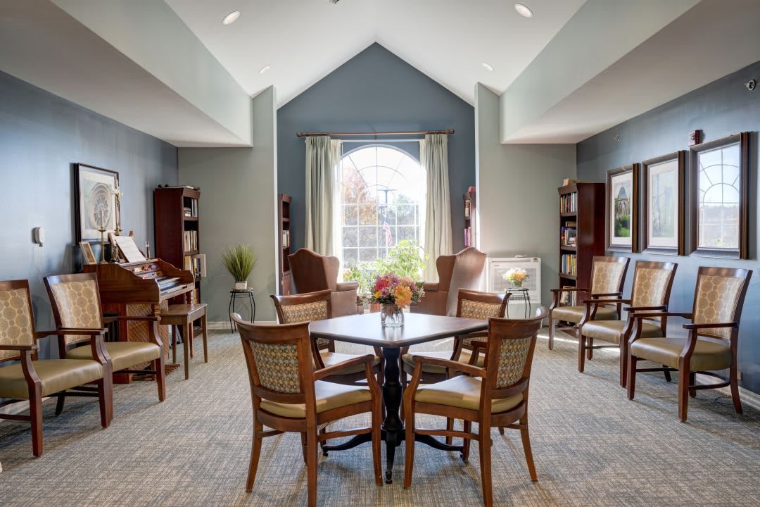 A well-lit room with a table and chairs, featuring a large window and elegant decor.