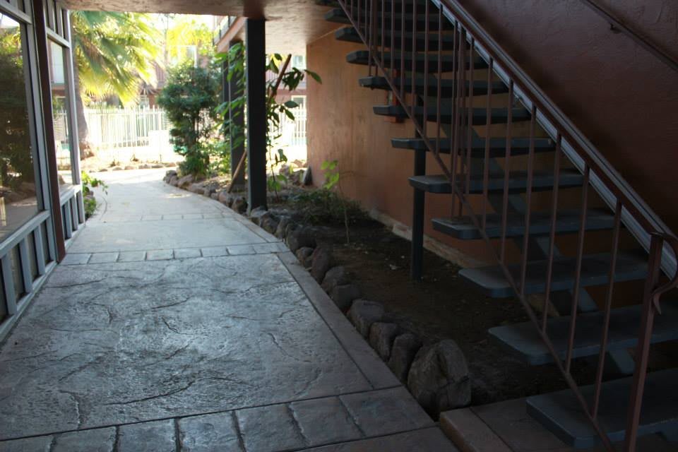 A shaded outdoor walkway featuring a spiral staircase and lush plants along the path.