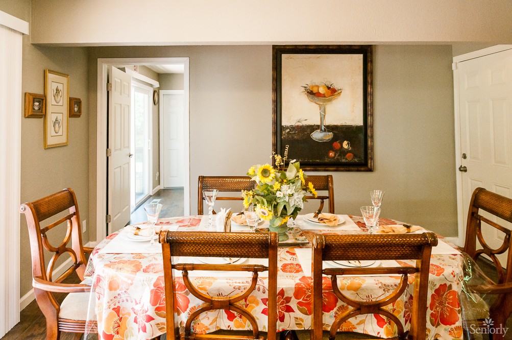 A well-decorated dining room with a floral tablecloth and a vase of flowers on the table.