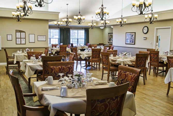 An elegant dining room setup with neatly arranged tables and chairs, featuring ornate chandeliers.