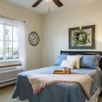 A cozy bedroom with a neatly made bed, wall clock, and decorative wreath on the wall.