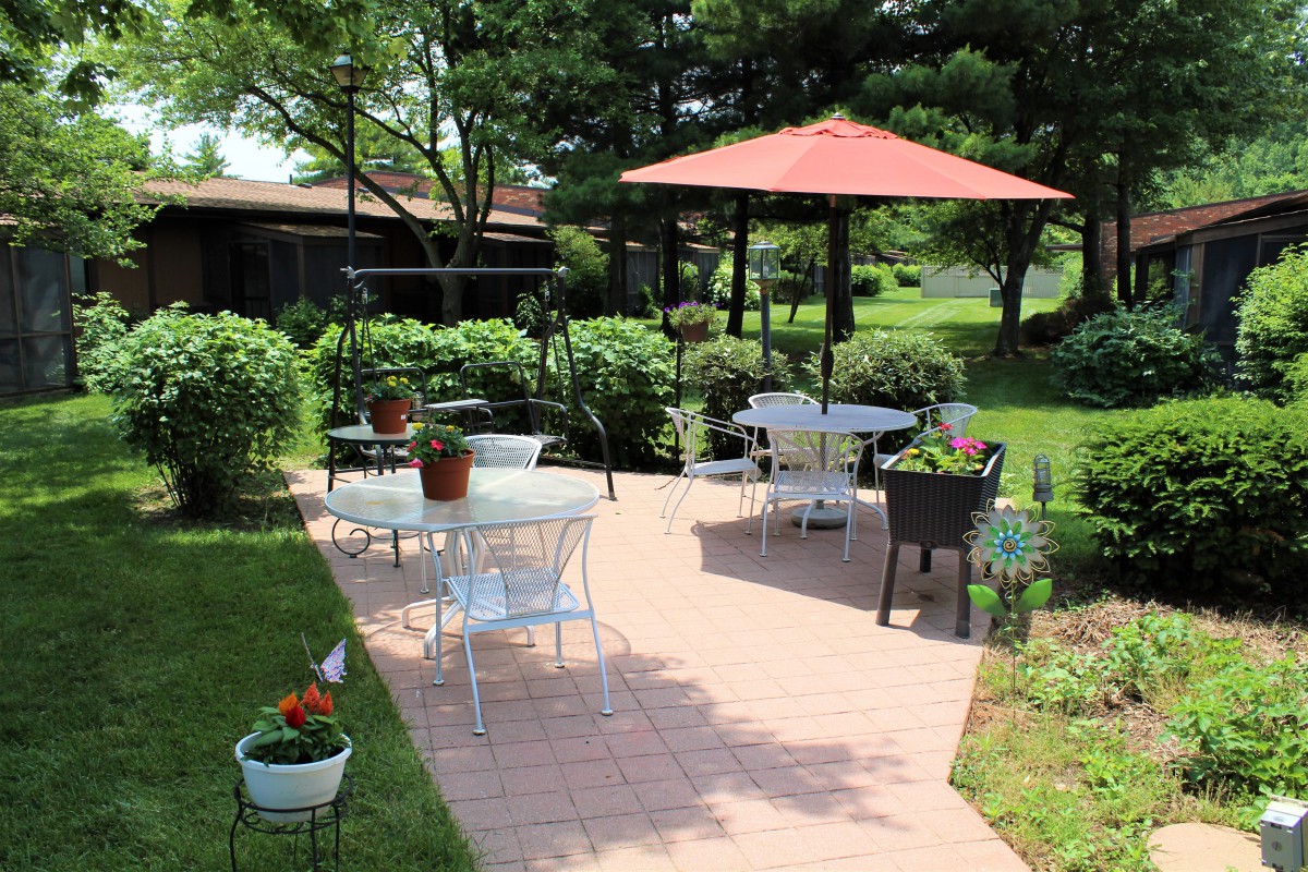 A sunny garden patio with outdoor seating and a large umbrella, surrounded by lush greenery.
