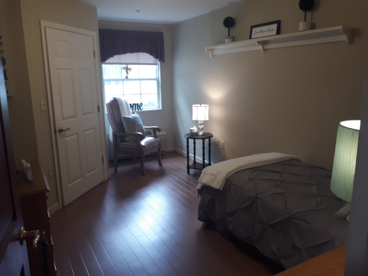 A cozy bedroom with a bed, chair, and lit lamp near a window.