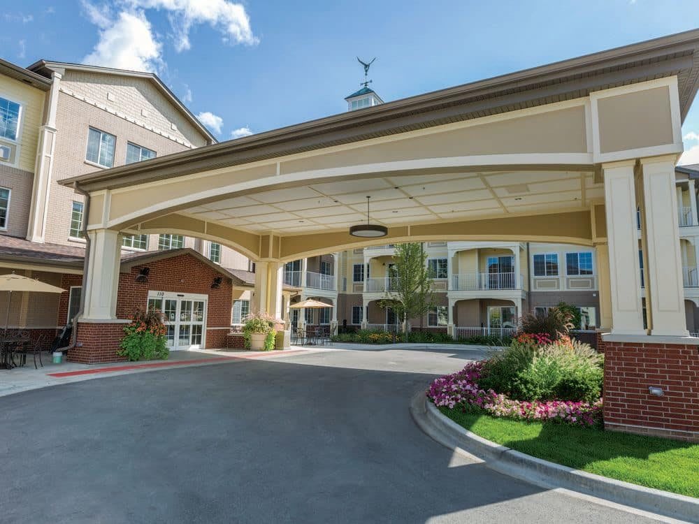 A well-landscaped building entrance with a covered driveway and flower beds.