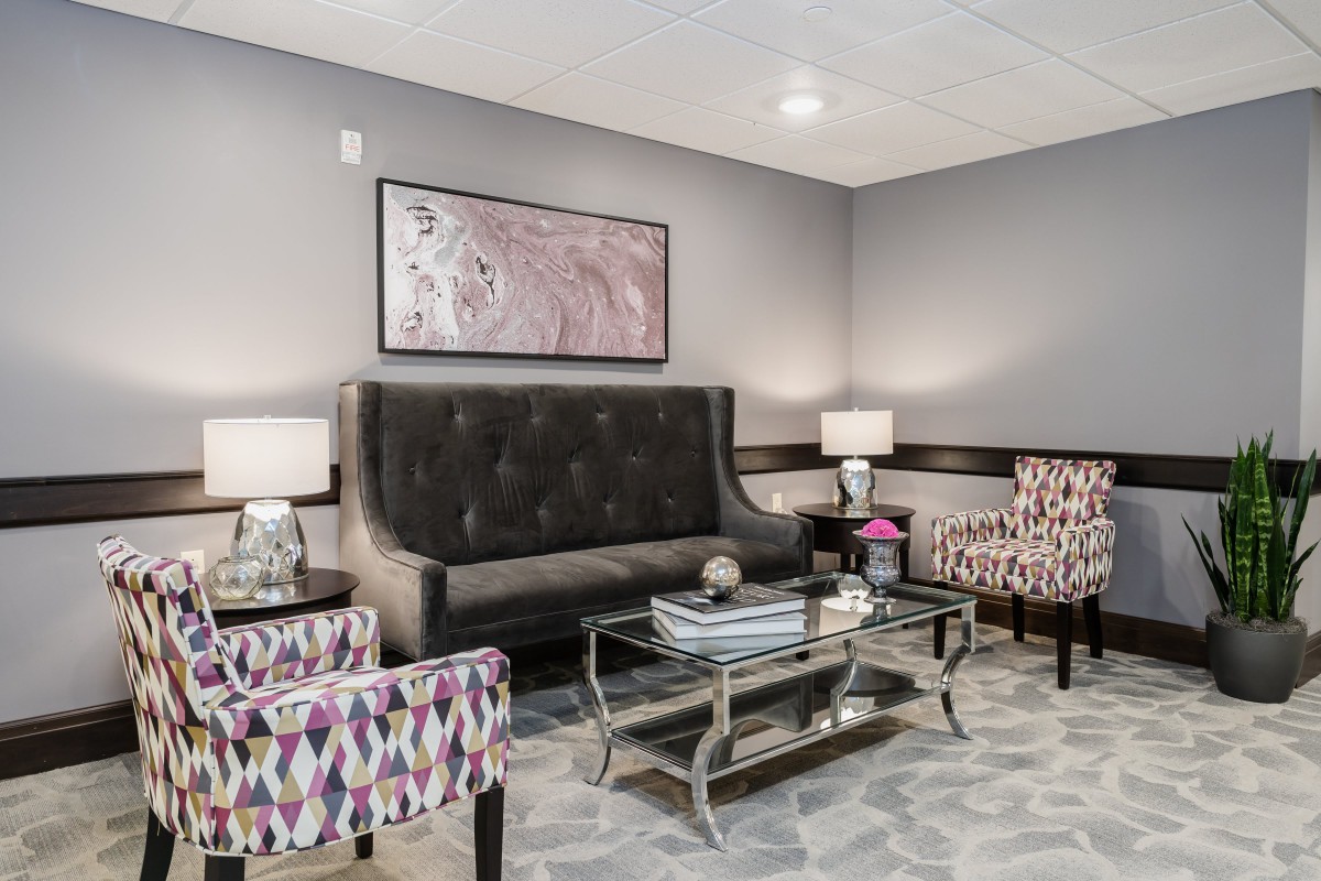 A modern living room with a dark sofa, patterned chairs, and a glass coffee table.