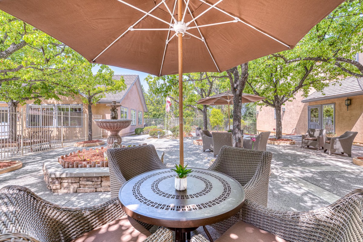 A tranquil outdoor patio area with a table, chairs, and umbrellas on a sunny day.