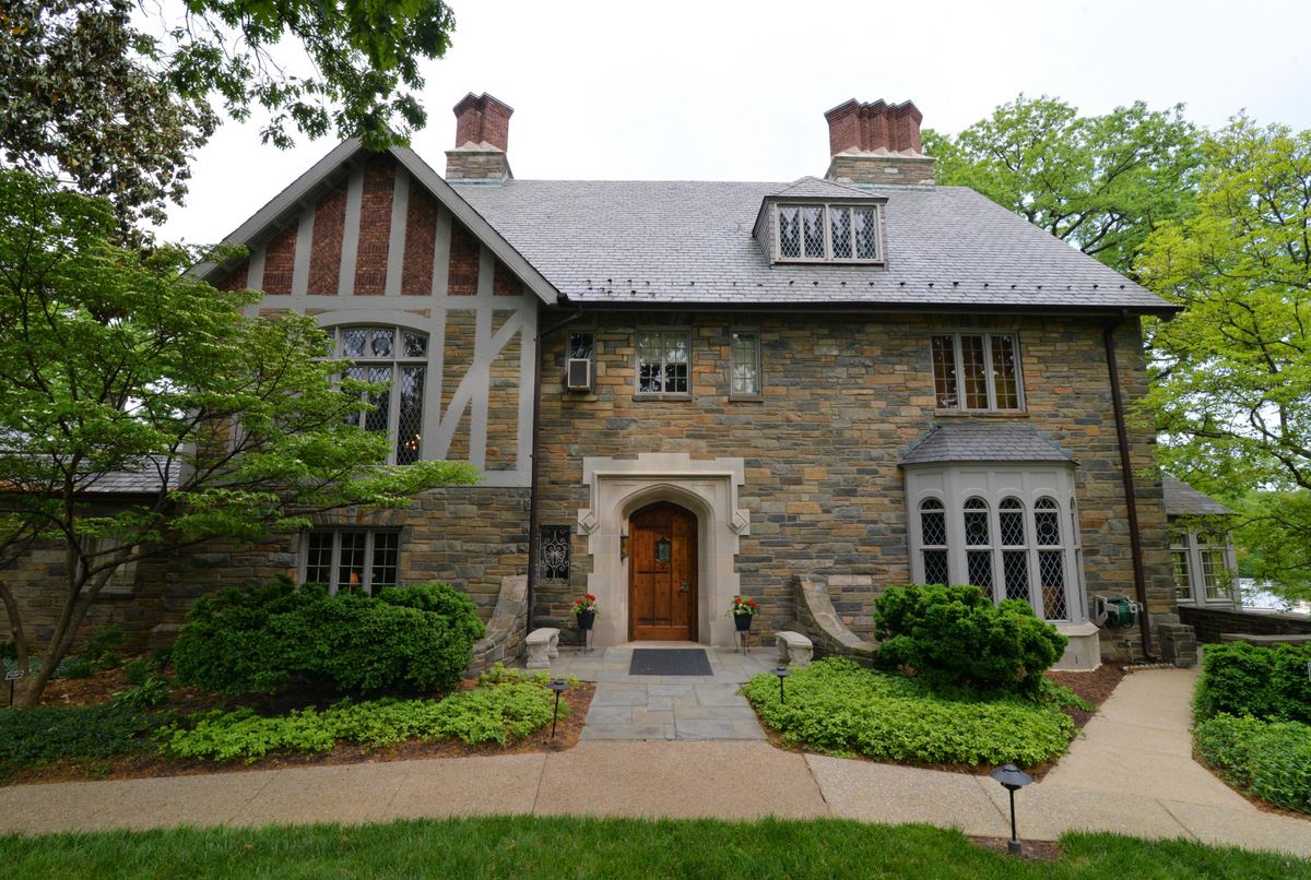 A charming stone Tudor-style house with well-maintained landscaping and prominent chimneys.