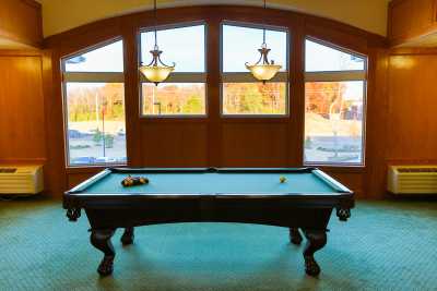 A billiards table in a game room with large windows and chandeliers.