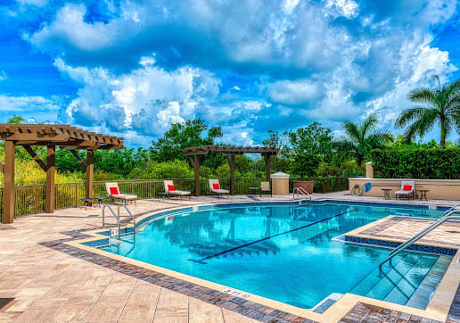 A scenic view of a luxurious swimming pool surrounded by lush greenery and a partly cloudy sky.
