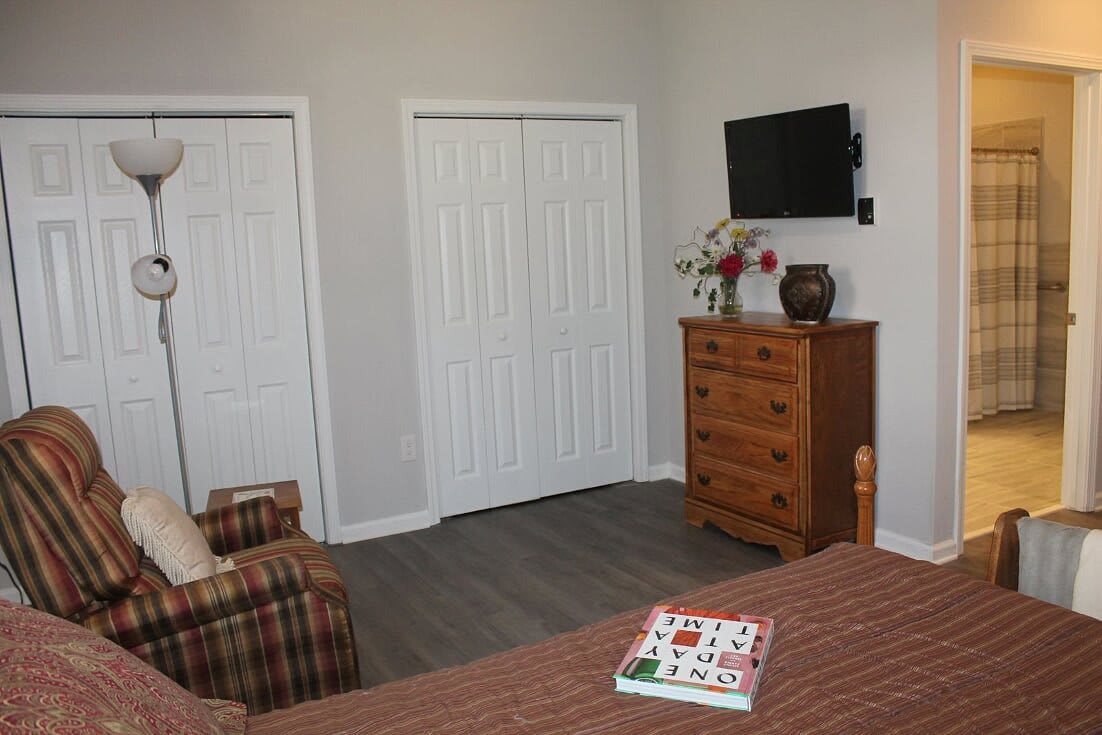 A cozy bedroom featuring a dresser, wall-mounted television, and closet doors.