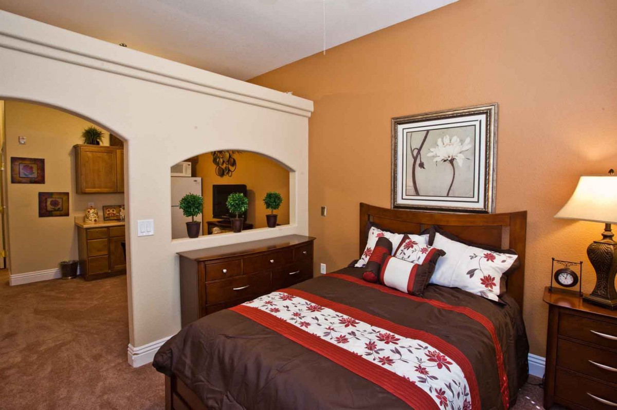 A cozy bedroom featuring a well-made bed with patterned pillows, warm-toned walls, and elegant decor.