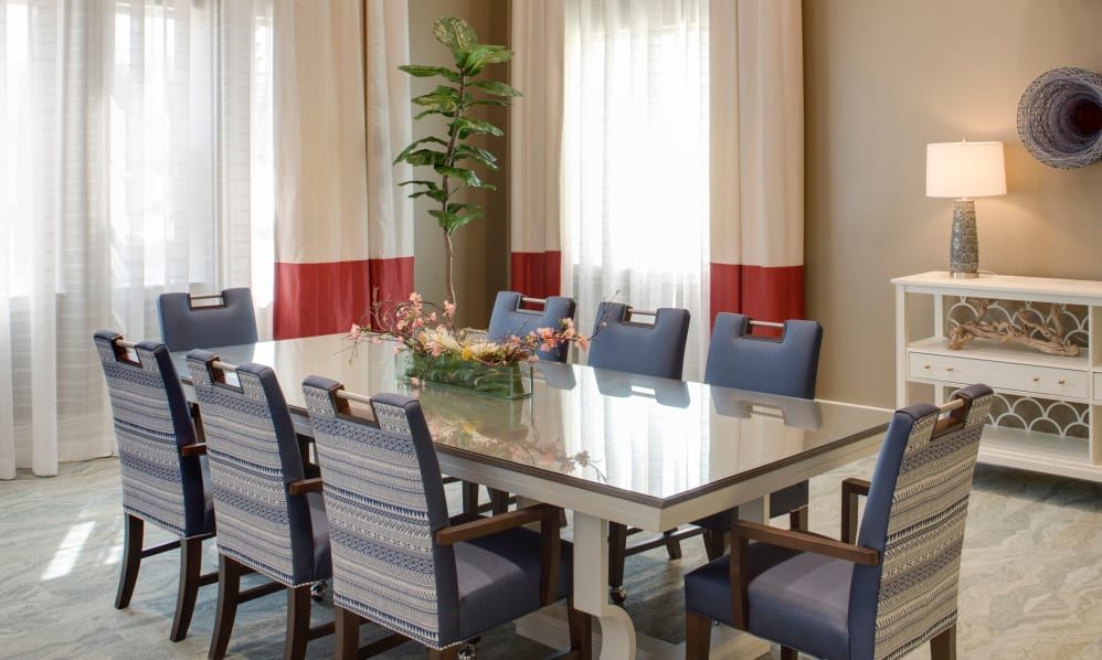 A beautifully decorated dining room with a large table, blue chairs, and elegant curtains.