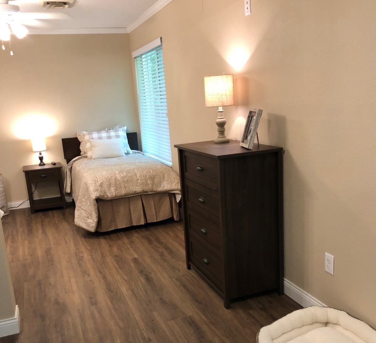 A cozy bedroom featuring a bed, dresser, and soft lighting.