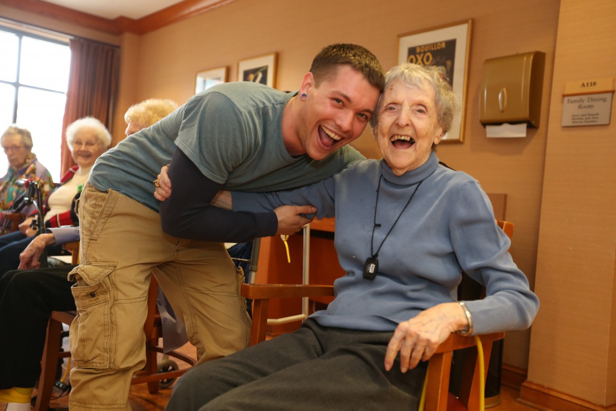 A joyful moment shared between a young man and an elderly woman in a care home setting.