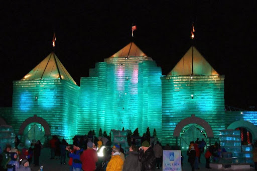 A beautifully lit ice castle during a winter festival, showcasing vibrant colors against the night sky.